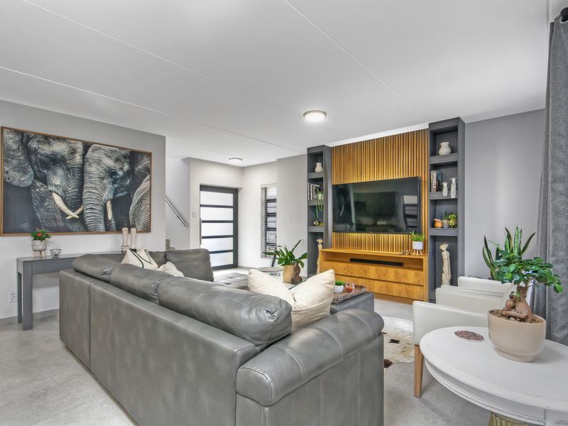 Modern open-plan living area featuring a custom built-in media wall with timber slat detailing and integrated shelving, complemented by neutral tiled flooring.