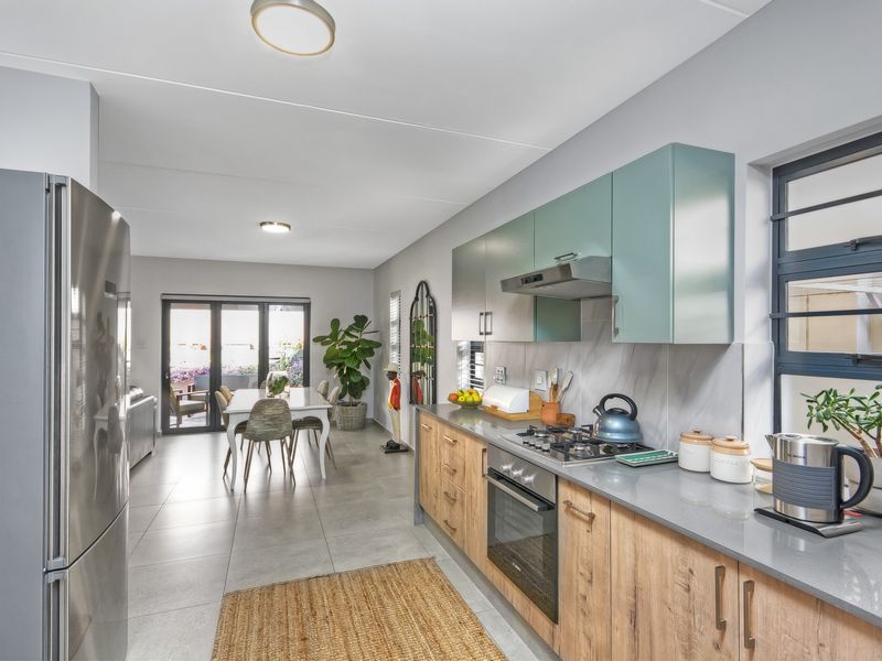 Modern open-plan kitchen and dining area featuring sleek cabinetry, stone countertops, built-in oven, gas hob, and direct access to the outdoor patio.
