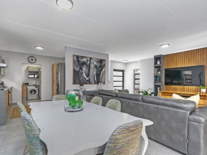 Open-plan living and dining area featuring modern cabinetry, a built-in media wall with timber slat detailing, and tiled flooring throughout.