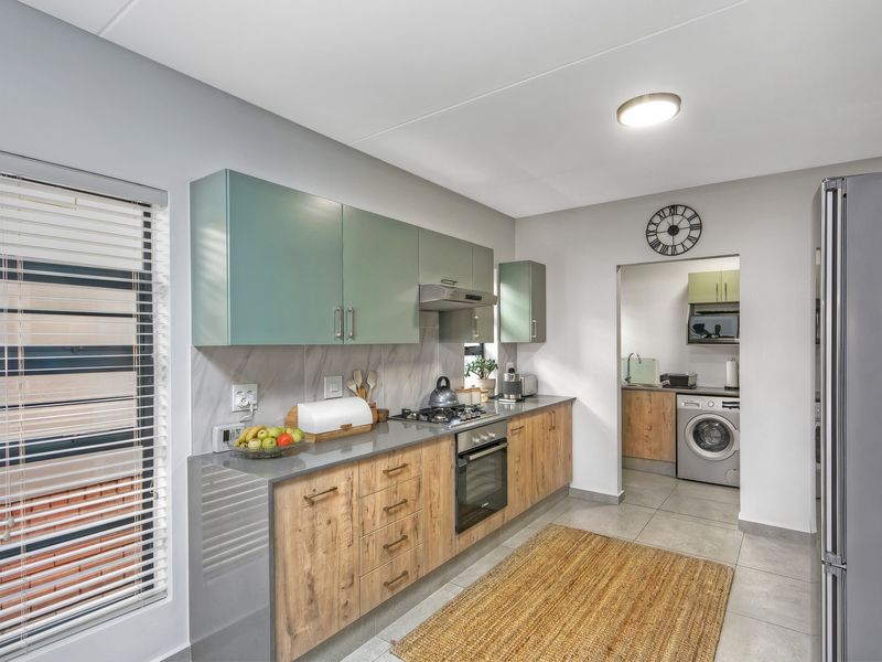 Modern kitchen featuring wood-grain lower cabinetry, sage green upper cabinets, stone countertops, built-in oven, gas hob, and an adjacent scullery area.