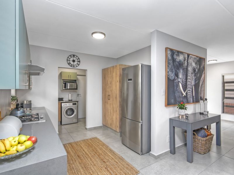 Modern kitchen featuring sleek cabinetry, stone countertops, integrated gas hob, and an adjacent scullery area with laundry facilities.