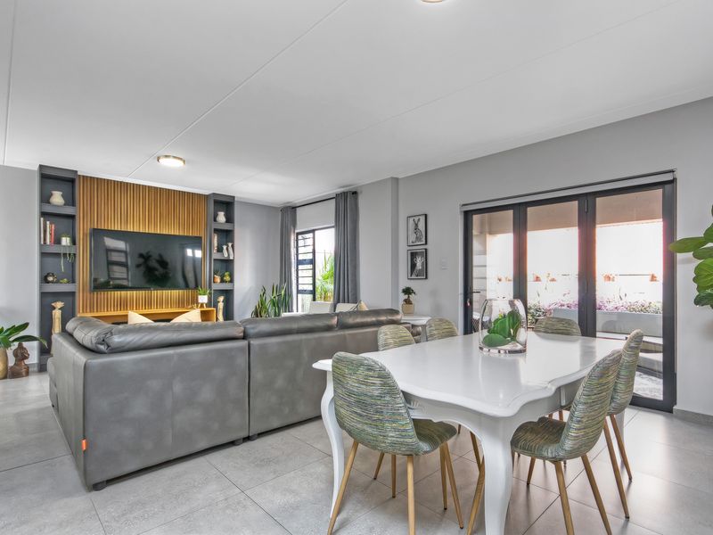 Spacious open-plan living and dining area featuring modern tiled flooring, a custom built-in media wall with shelving, and large glass doors leading to the patio.