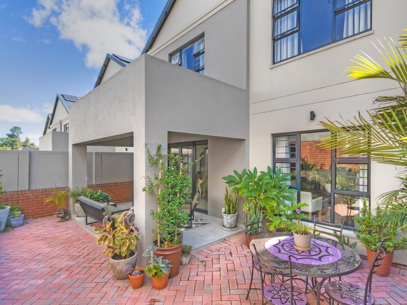 A well-maintained rear exterior view of the townhouse featuring a covered patio area with brick paving and large windows.