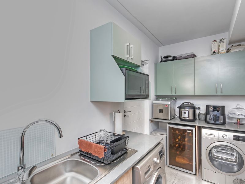 Compact laundry room featuring built-in cabinetry, stainless steel sink, and dedicated spaces for laundry appliances.