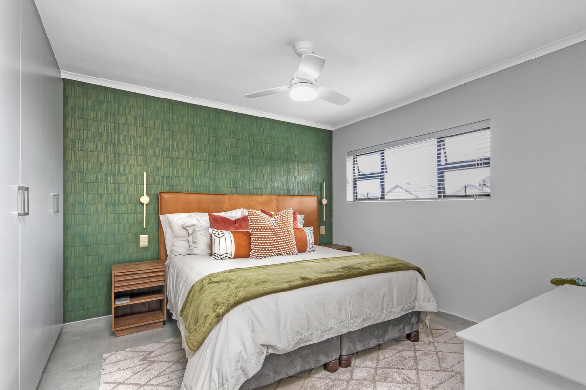 A well-presented bedroom featuring built-in cupboards, a ceiling fan, and a decorative feature wall with integrated lighting.