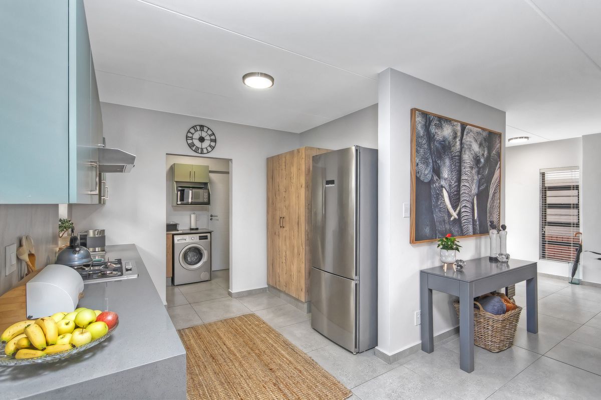 Modern kitchen featuring sleek cabinetry, stone countertops, integrated gas hob, and an adjacent scullery area with laundry facilities.