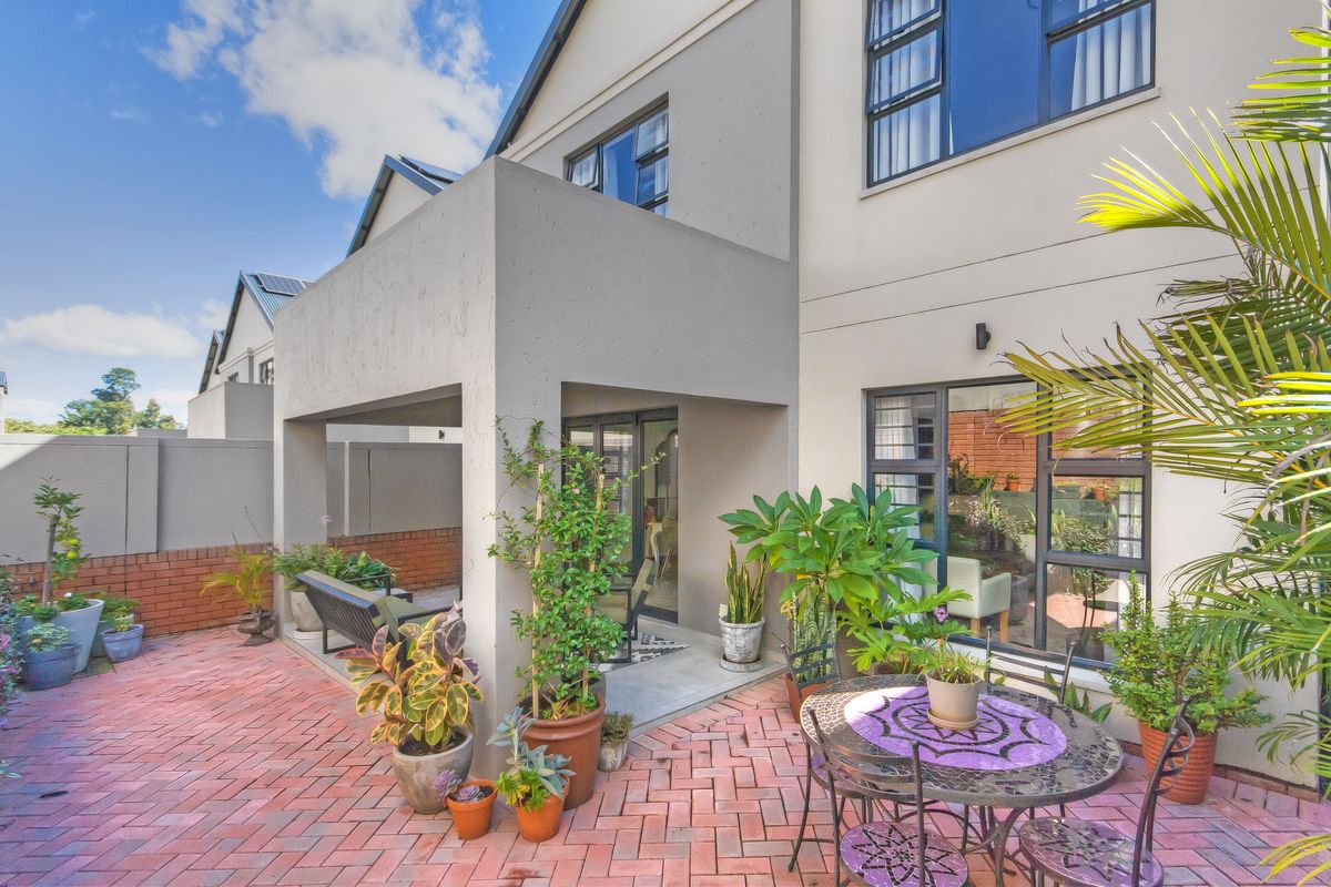 A well-maintained rear exterior view of the townhouse featuring a covered patio area with brick paving and large windows.