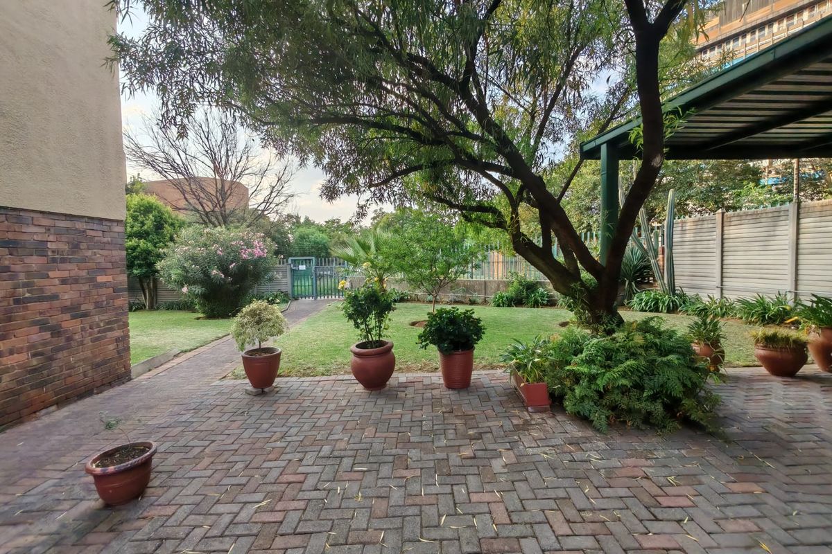 A private rear garden featuring a paved patio area, established trees, and a lawn, providing a pleasant outdoor space for relaxation.