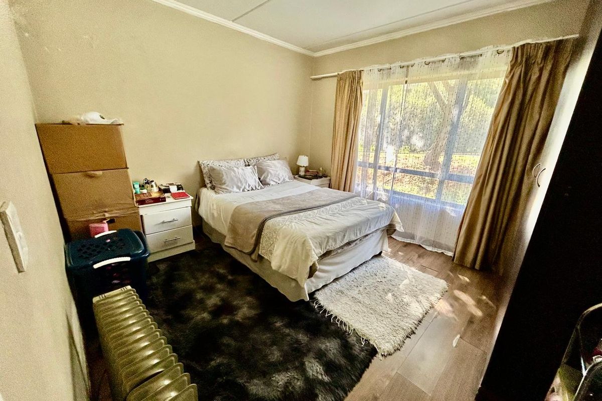 A standard bedroom featuring laminate flooring, a large window with curtain tracks, and neutral wall finishes.