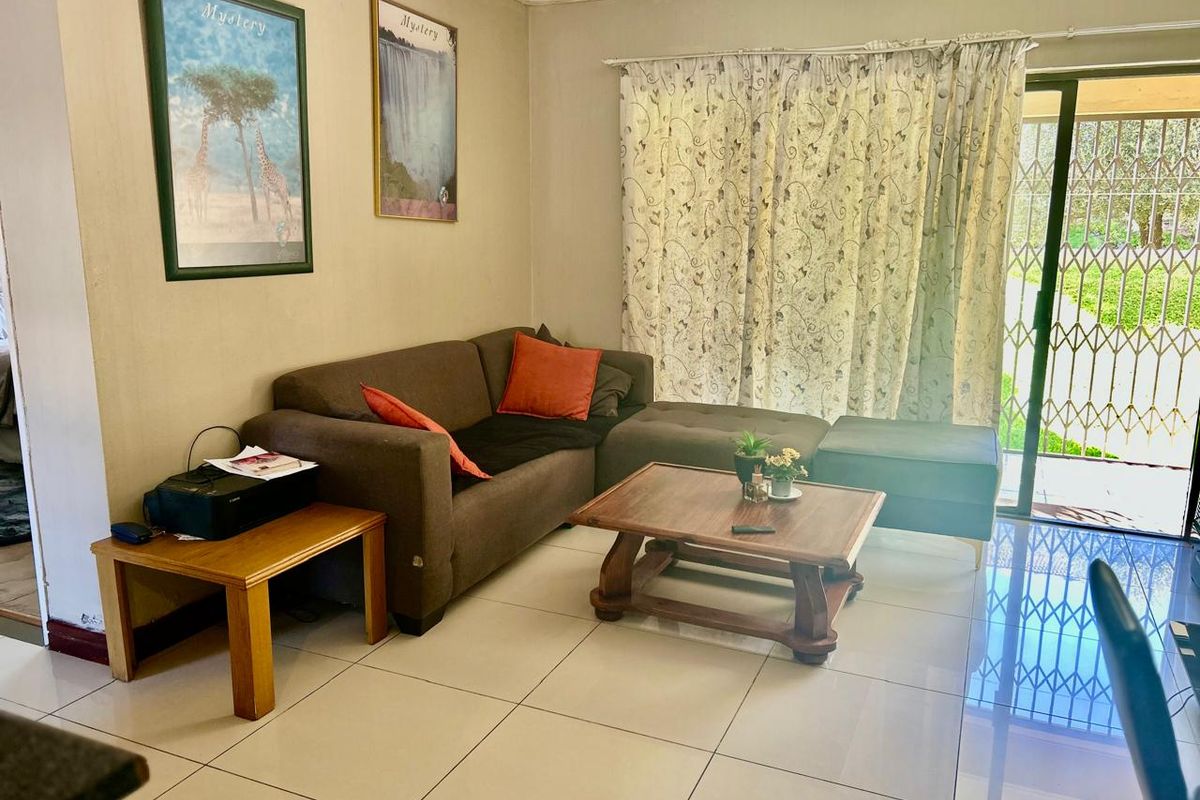 A living room featuring large floor tiles and a sliding glass door with security gate leading to an outdoor area.