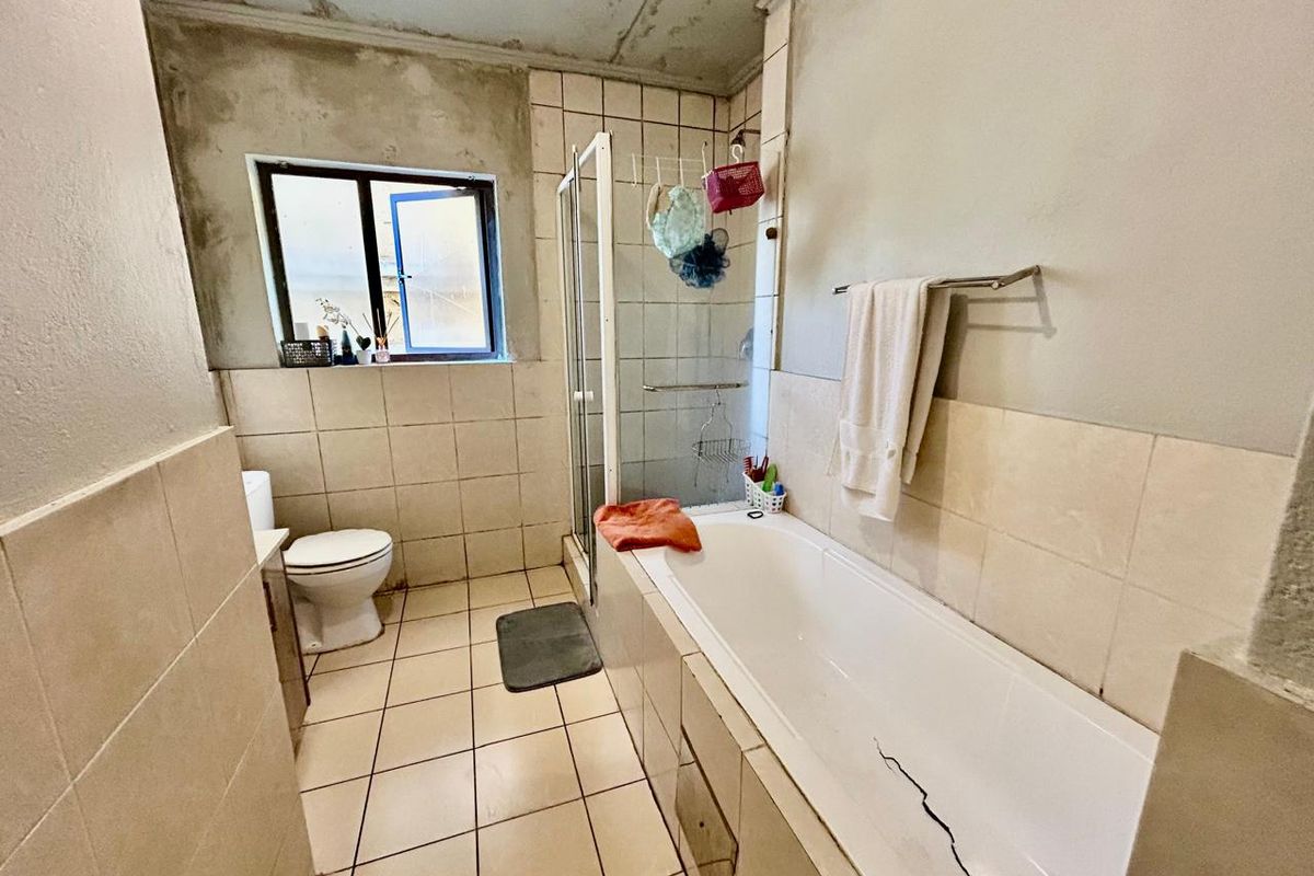 A dated bathroom featuring a shower enclosure, bathtub, and toilet, currently requiring significant renovation and repair to the walls, ceiling, and bathtub.