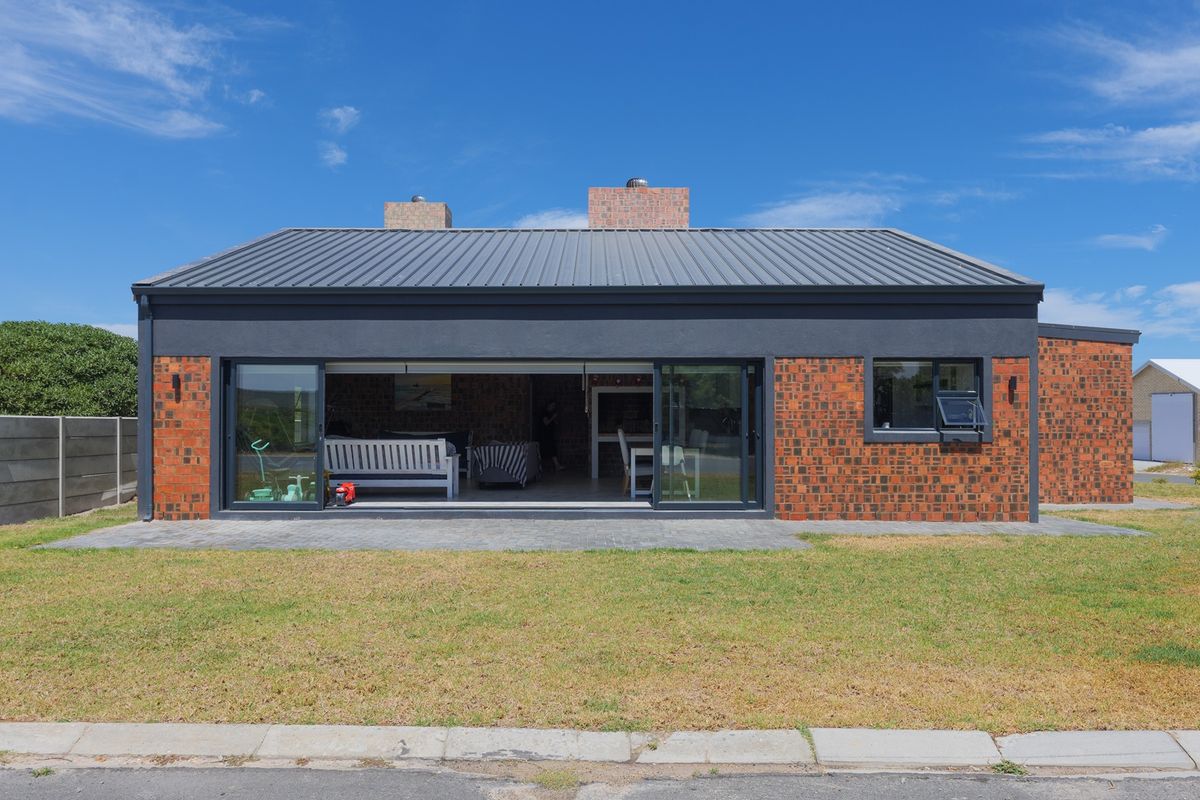 Rear view of a modern house featuring a metal roof, exposed brickwork, and large sliding glass doors opening onto a paved patio area.