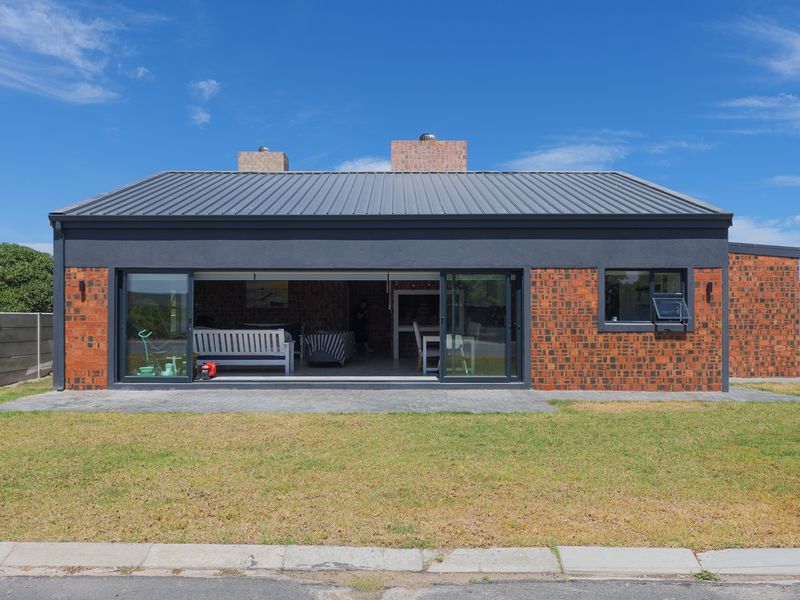 Rear view of a modern house featuring a metal roof, exposed brickwork, and large sliding glass doors opening onto a paved patio area.