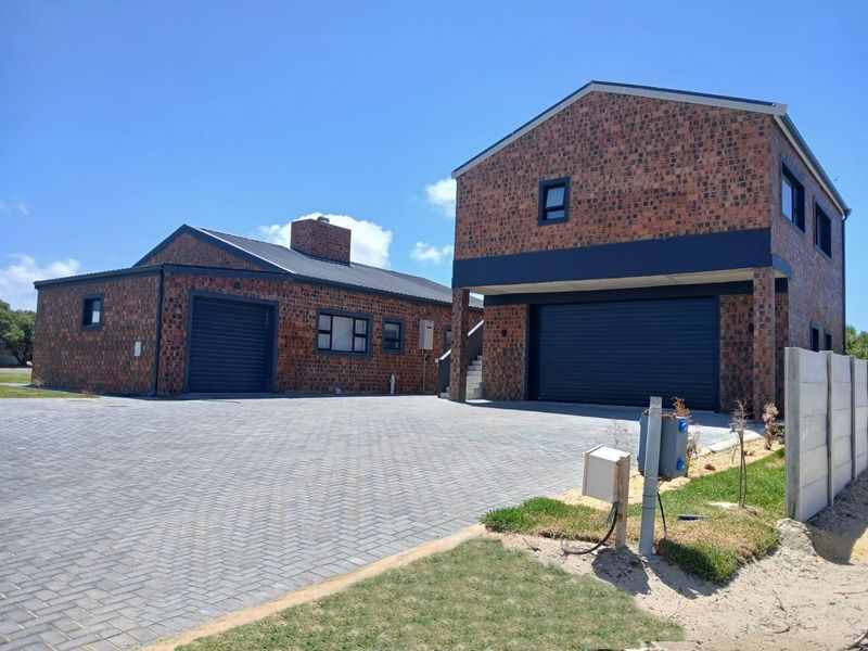 Modern face brick house featuring a spacious paved driveway, double garage, and clean architectural lines under a clear blue sky.