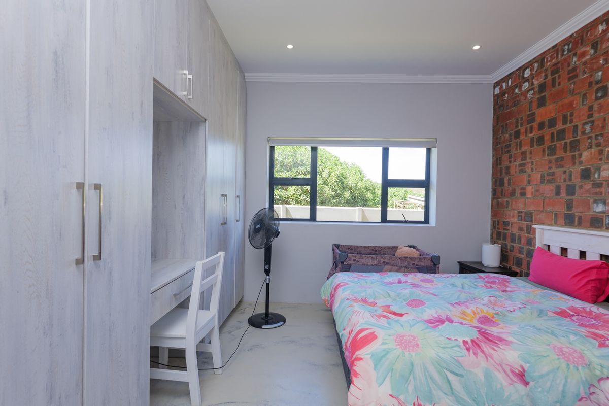A well-maintained bedroom featuring a striking exposed brick feature wall, extensive built-in cabinetry with an integrated desk, and modern aluminium window frames.