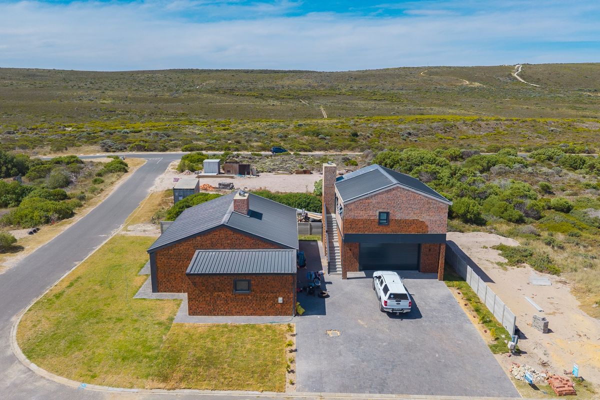 Aerial view of a two-story brick house with a metal roof, paved driveway, and surrounding natural landscape.