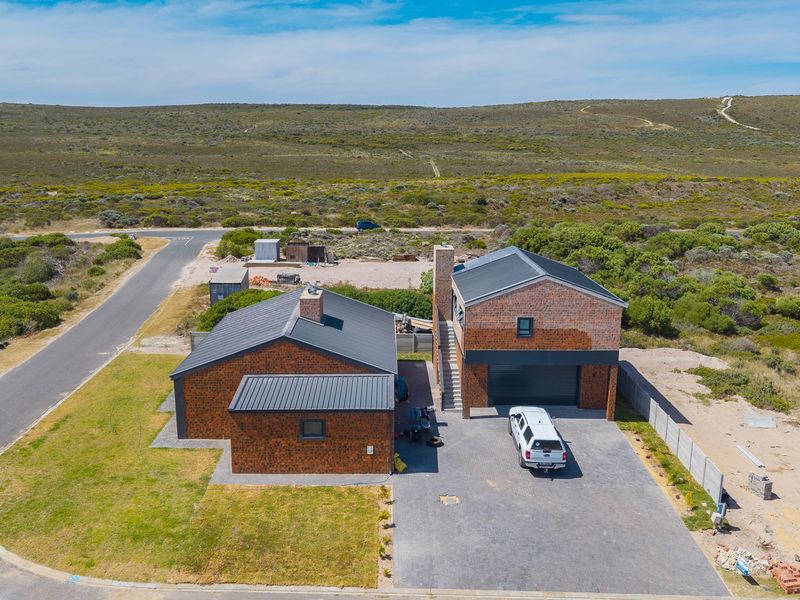Aerial view of a two-story brick house with a metal roof, paved driveway, and surrounding natural landscape.