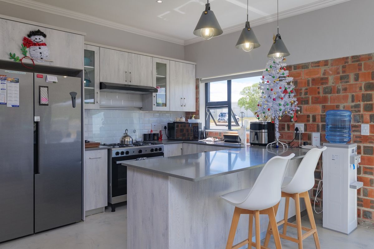 Modern kitchen featuring light wood-grain cabinetry, stone countertops, a central island, and a striking exposed brick feature wall with subway tile backsplash.