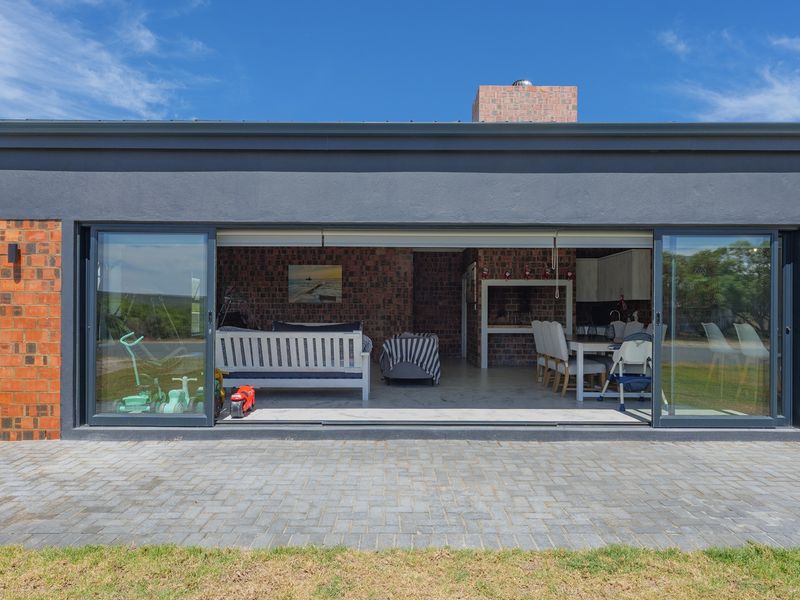 A covered outdoor patio area featuring large sliding glass doors, exposed brick walls, and a built-in braai, seamlessly connecting to the paved garden space.