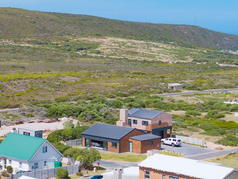 Aerial view of a modern residential property featuring a metal roof, brick exterior, and paved driveway, situated in a coastal landscape.