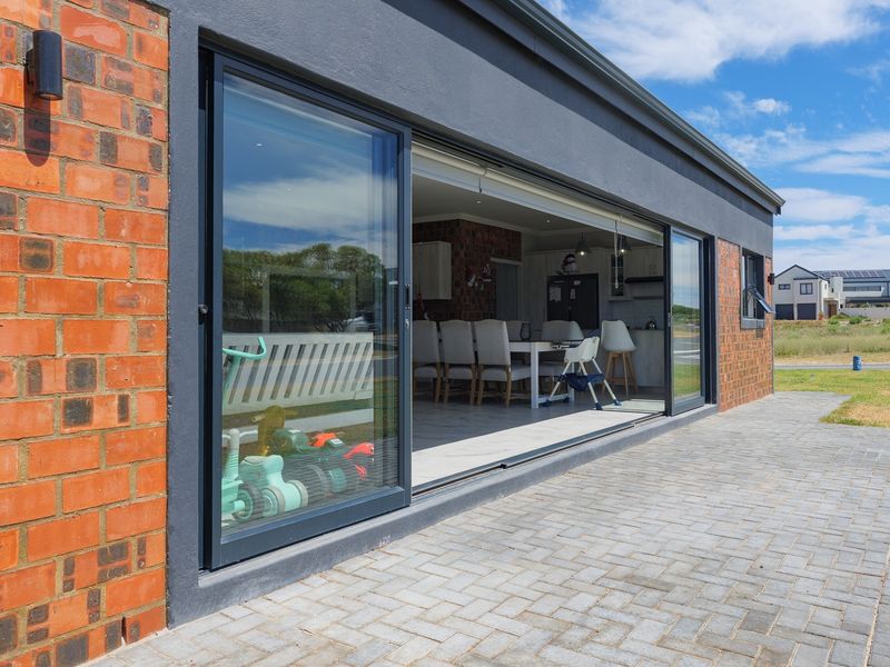 A modern exterior view featuring a paved patio area with large sliding glass doors opening into an open-plan living space.