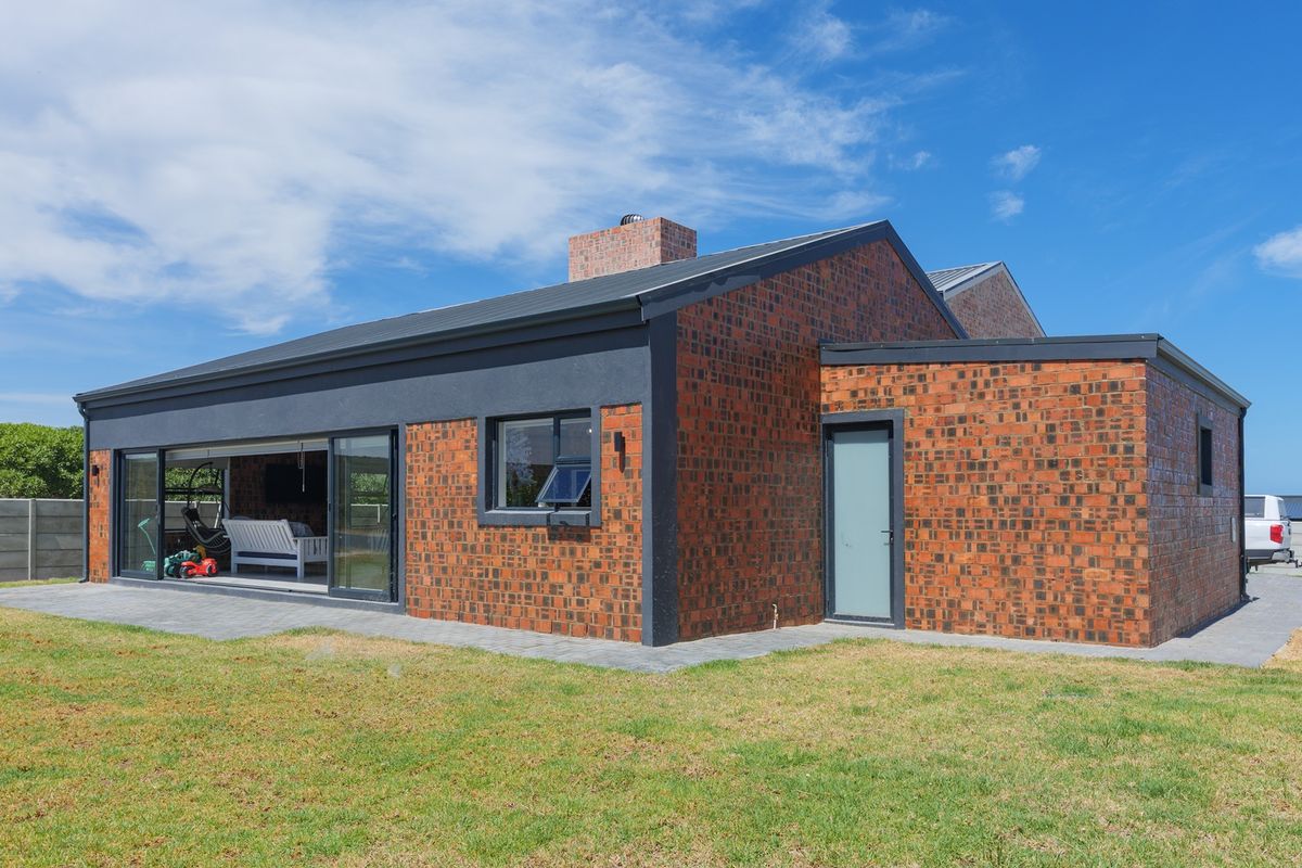 Rear view of a modern house featuring exposed brickwork, large sliding glass doors opening to a paved patio, and a well-maintained garden.