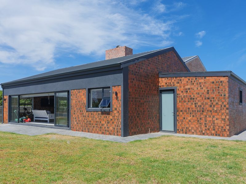 Rear view of a modern house featuring exposed brickwork, large sliding glass doors opening to a paved patio, and a well-maintained garden.