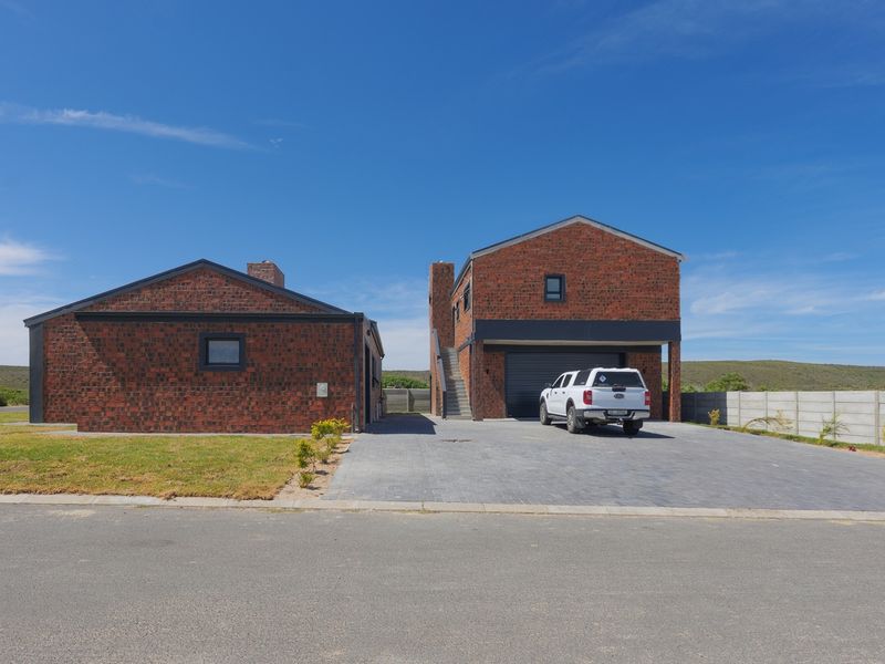 Front view of a modern double-story brick house featuring a paved driveway, integrated garage, and external staircase leading to the upper level.