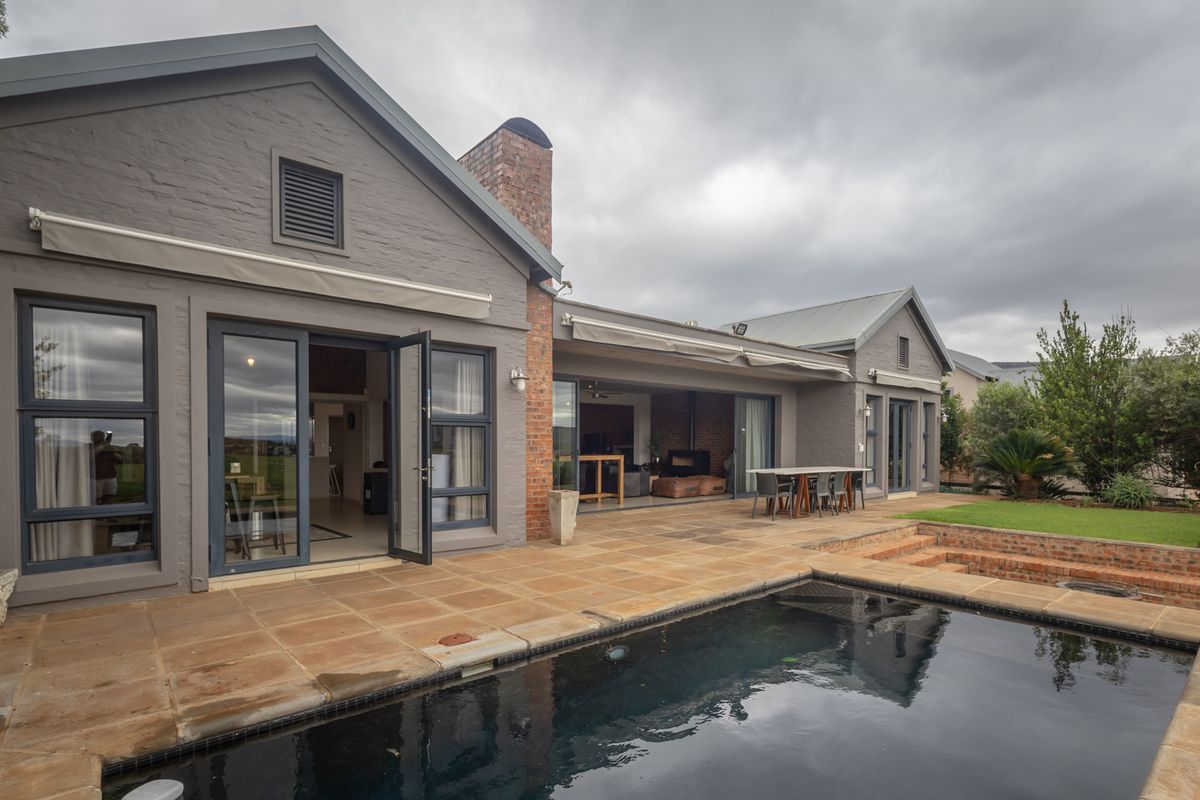 Rear exterior view featuring a paved patio area, swimming pool, brick chimney, and seamless indoor-outdoor flow through large aluminium doors.