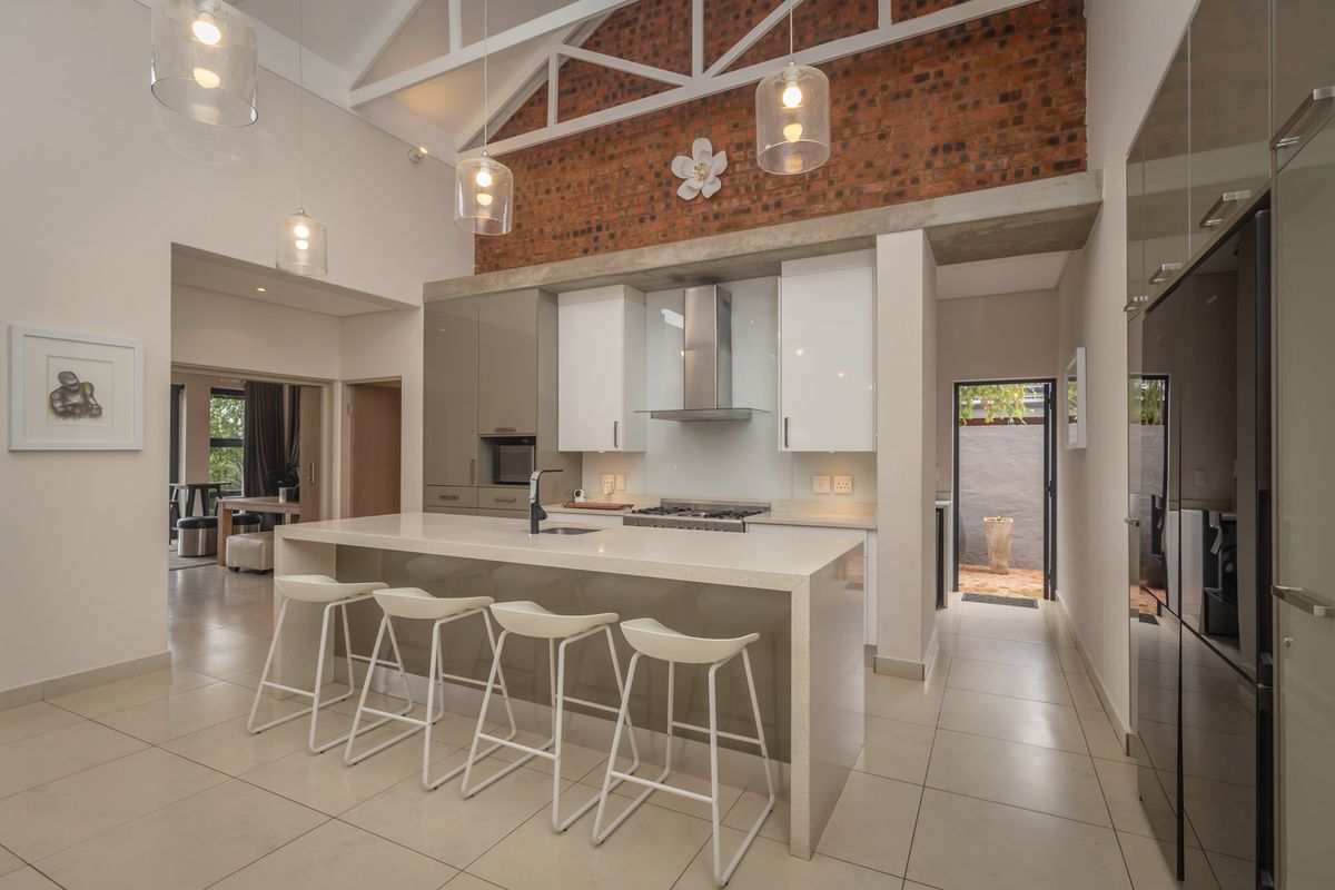 Modern kitchen featuring a large island with stone countertops, exposed brick wall, high vaulted ceilings with exposed trusses, and sleek built-in cabinetry.