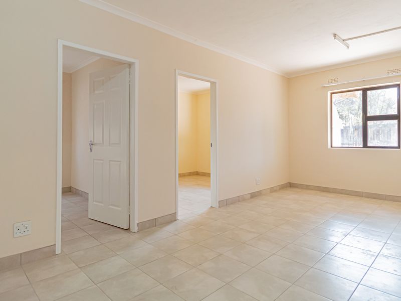 A bright, empty living area featuring neutral tiled floors, clean walls, and access to adjacent rooms through internal doorways.