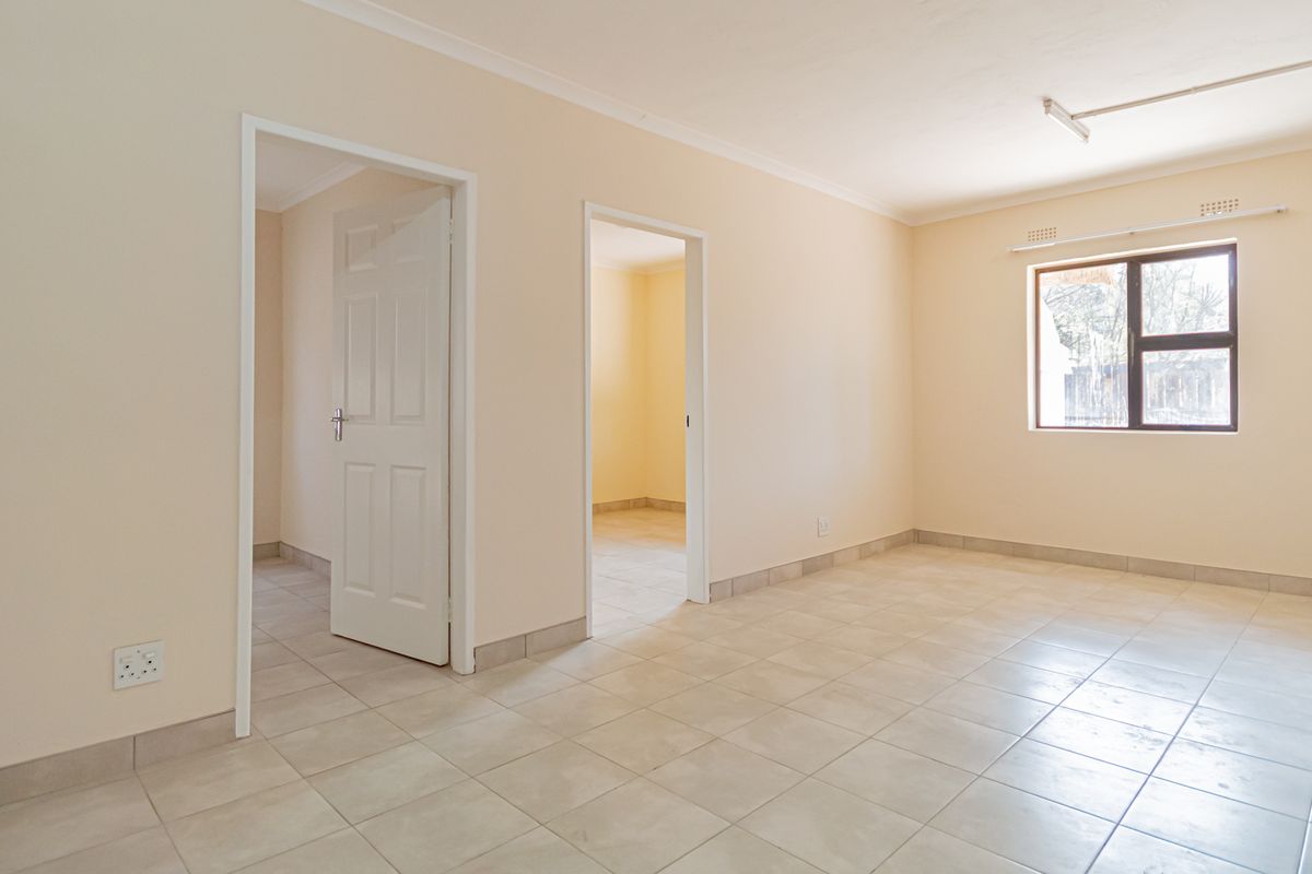 A bright, empty living area featuring neutral tiled floors, clean walls, and access to adjacent rooms through internal doorways.