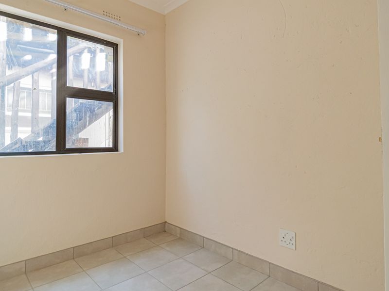 An empty bedroom featuring neutral tiled flooring, a single aluminium window, and a standard internal door, providing a blank canvas for interior design.