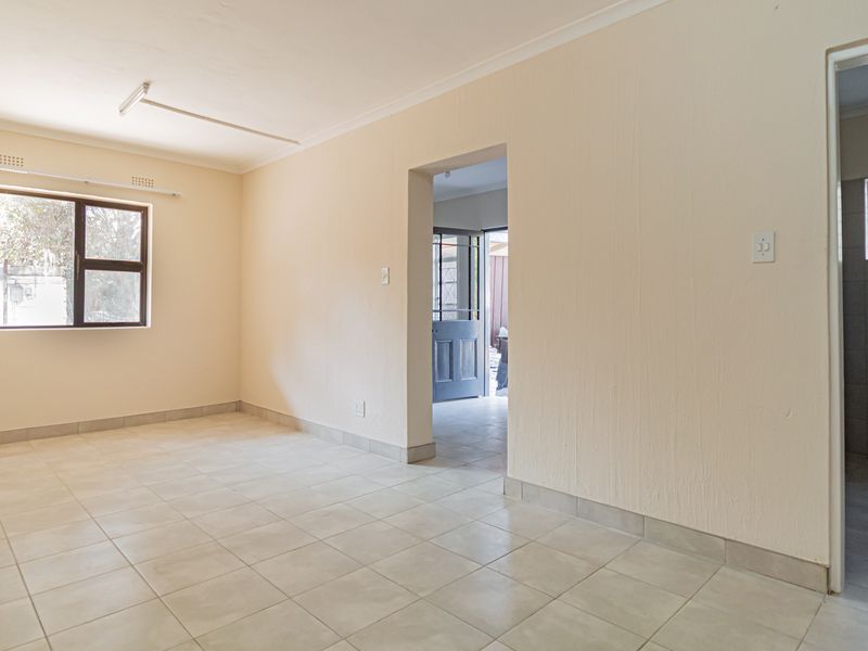 An empty, neutrally painted living area featuring tiled flooring, coving, and direct access to an adjacent room and bathroom.