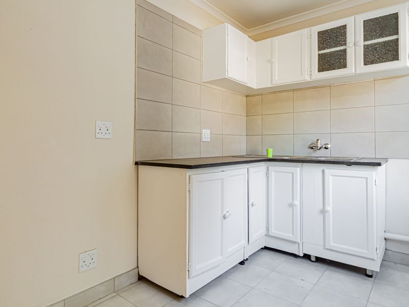 A compact kitchen area featuring white built-in cabinetry, a dark laminate countertop, and neutral tiled splashbacks, offering a functional space ready for updates.
