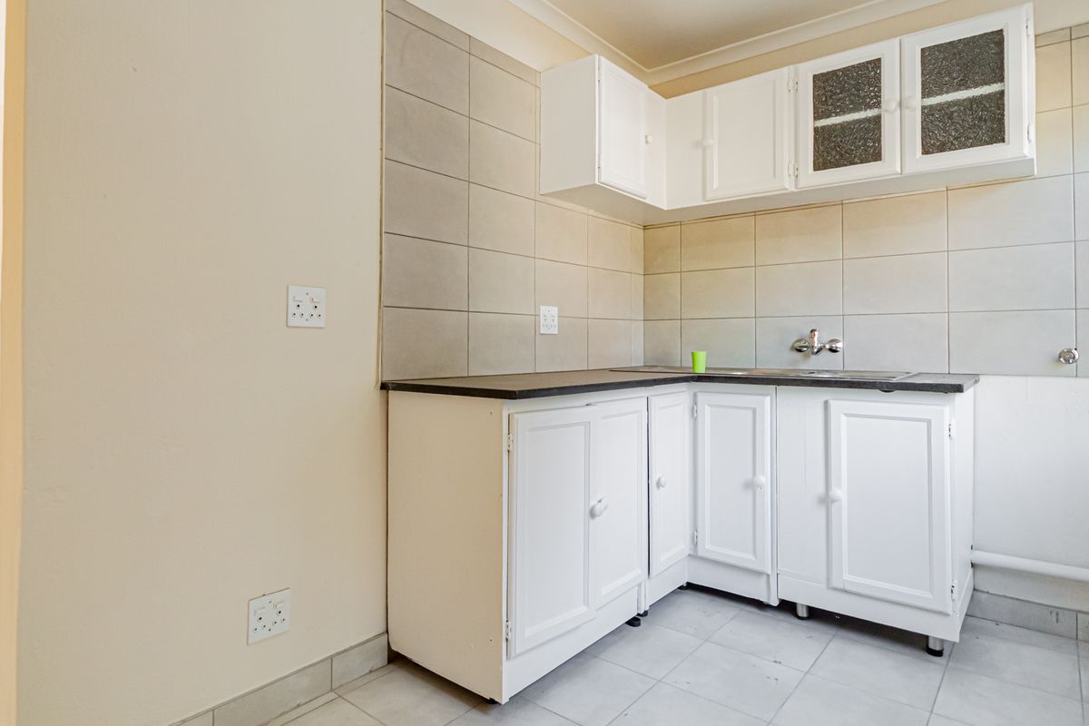 A compact kitchen area featuring white built-in cabinetry, a dark laminate countertop, and neutral tiled splashbacks, offering a functional space ready for updates.