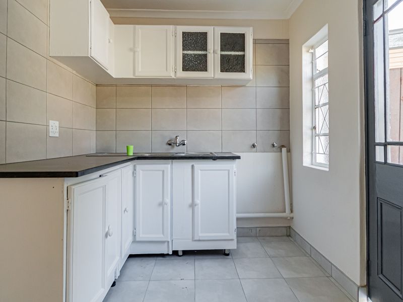 A functional scullery or laundry area featuring white built-in cabinetry, tiled splashbacks, and dedicated plumbing connections for appliances.