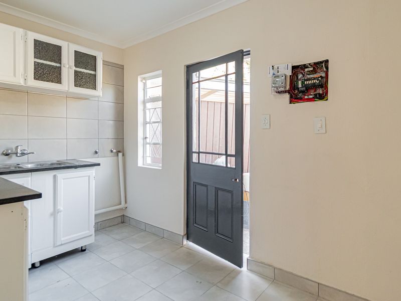 A functional scullery area featuring built-in cabinetry, a stainless steel sink, tiled finishes, and direct access to the exterior.