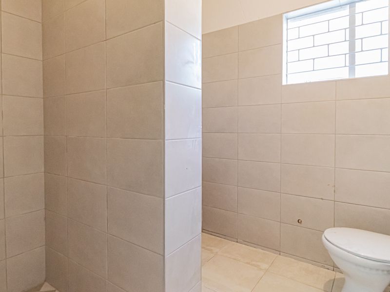 A functional, tiled bathroom featuring a standard toilet and a privacy window with security bars, presenting a clean and neutral space.