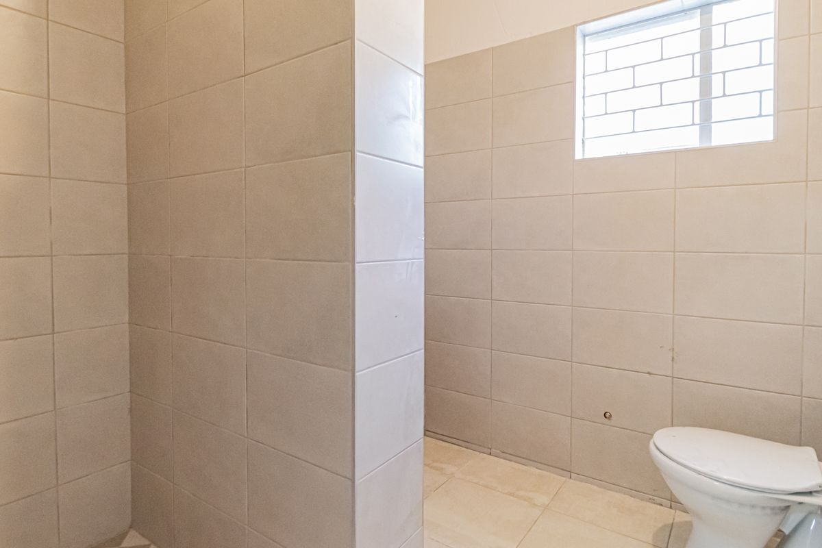 A functional, tiled bathroom featuring a standard toilet and a privacy window with security bars, presenting a clean and neutral space.
