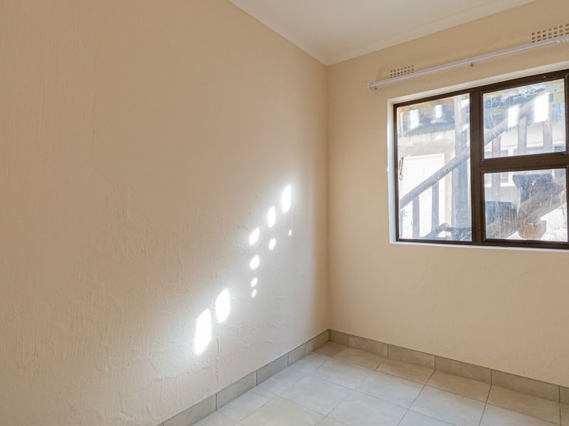 A bright, empty bedroom featuring neutral wall paint, tiled flooring, and an aluminium-framed window.