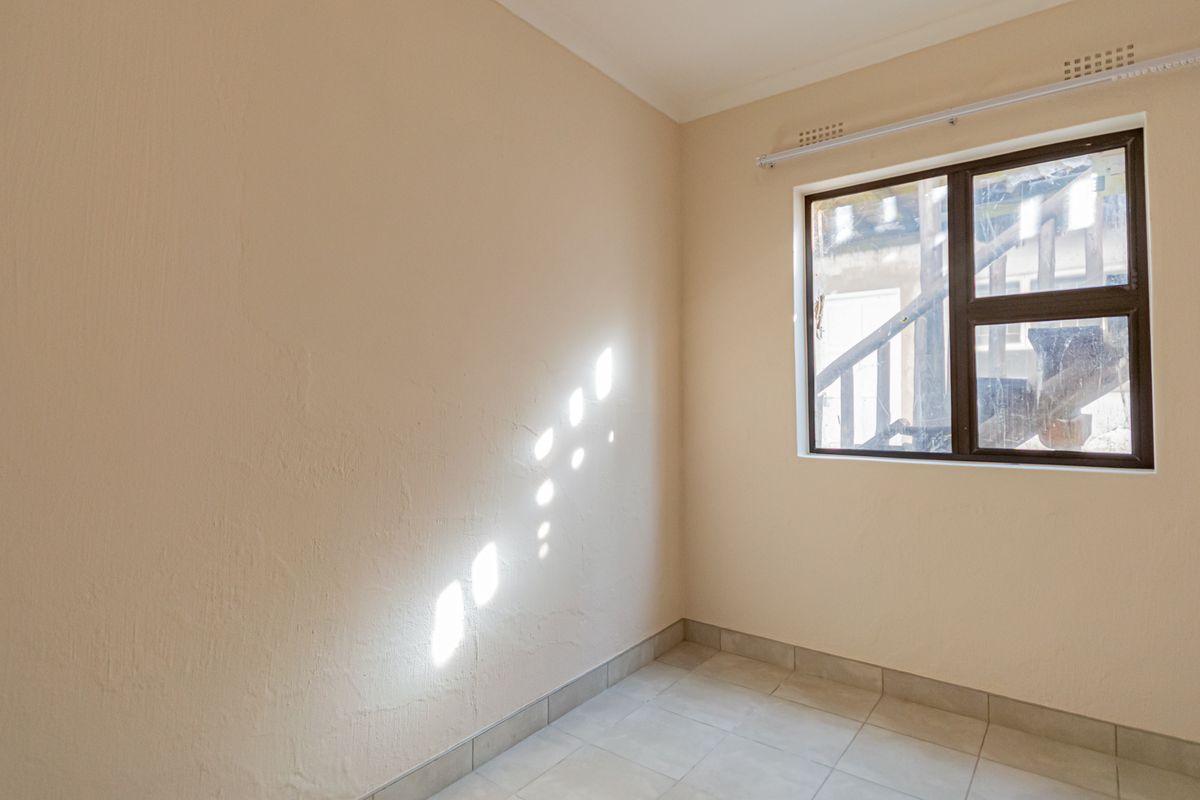 A bright, empty bedroom featuring neutral wall paint, tiled flooring, and an aluminium-framed window.