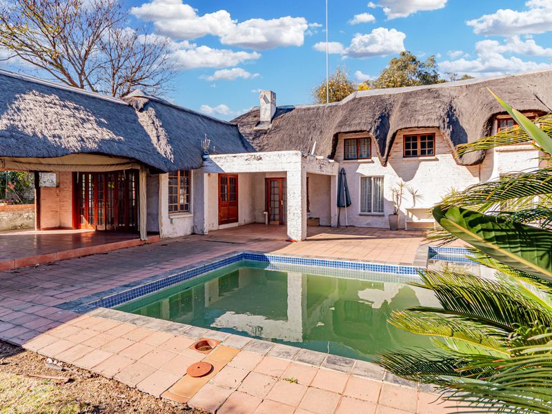 Rear exterior view of a cottage featuring a thatched roof, covered patio area, and a swimming pool requiring maintenance.