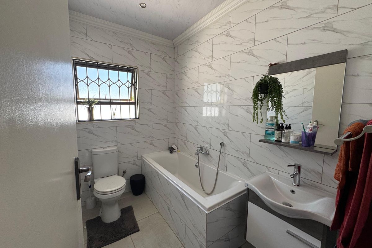 A modern bathroom featuring marble-look wall tiles, a built-in bathtub with shower mixer, a vanity basin, and a toilet.