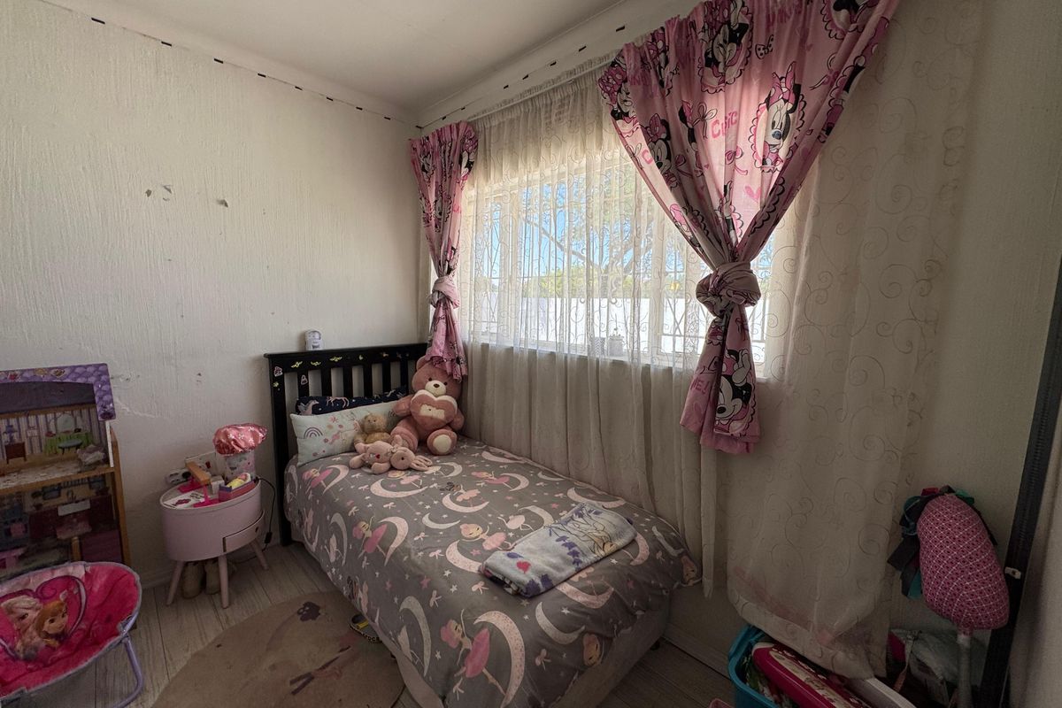 A compact bedroom featuring a large window with curtains, light-toned flooring, and textured wall finishes.