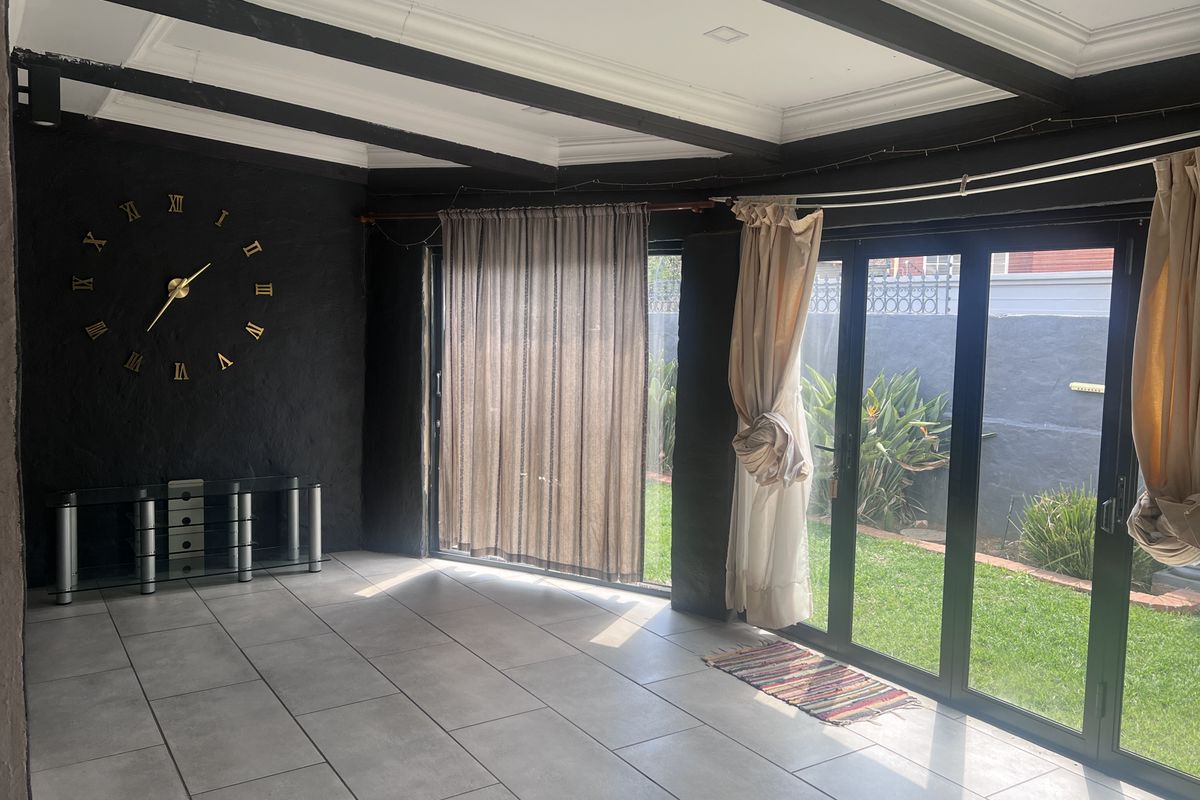 Spacious living area featuring dark accent walls, exposed ceiling beams, large tiled floors, and bi-fold glass doors providing direct access to the garden.