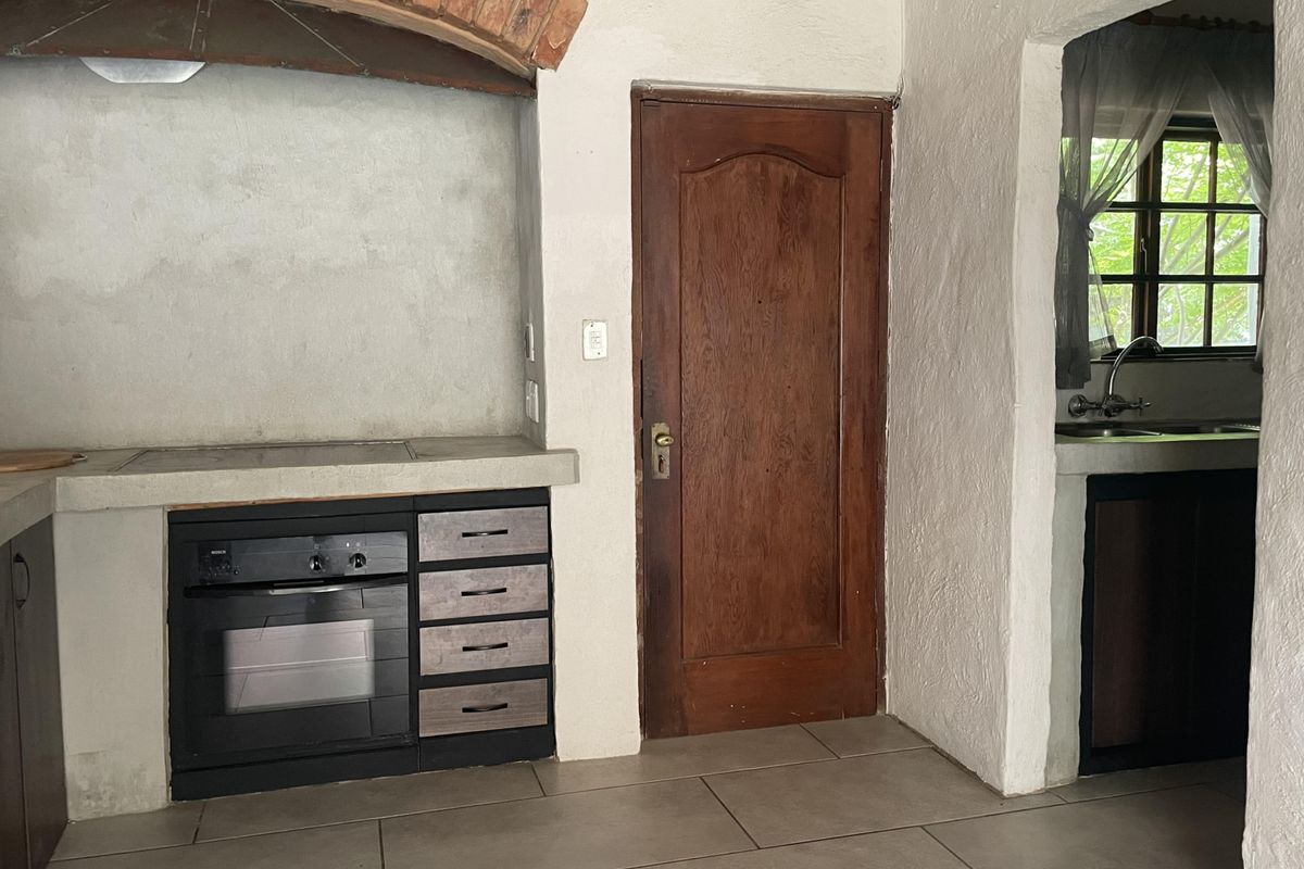 A rustic kitchen area featuring a brick arch over the cooking station, concrete countertops, built-in oven, and tiled flooring with an adjacent scullery area.