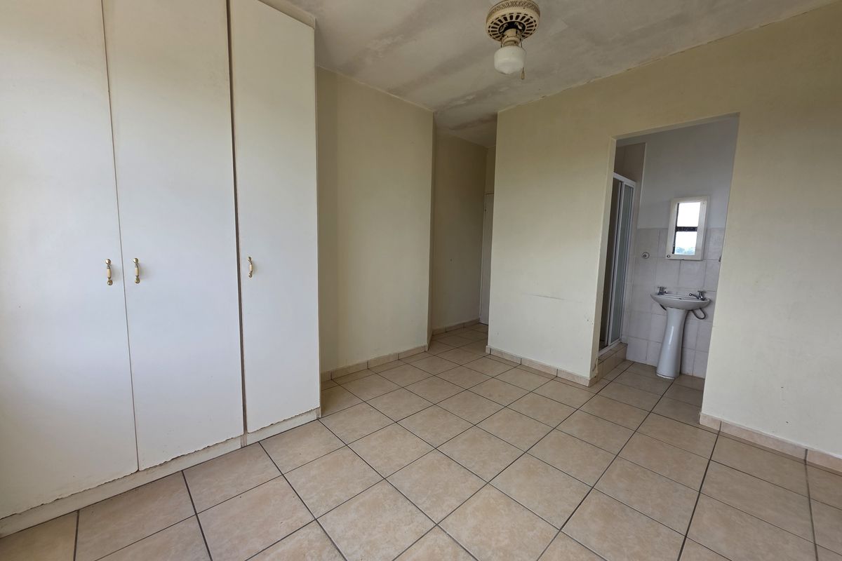 An empty bedroom featuring built-in cupboards, tiled flooring, and an en-suite bathroom area with a pedestal basin and shower cubicle.