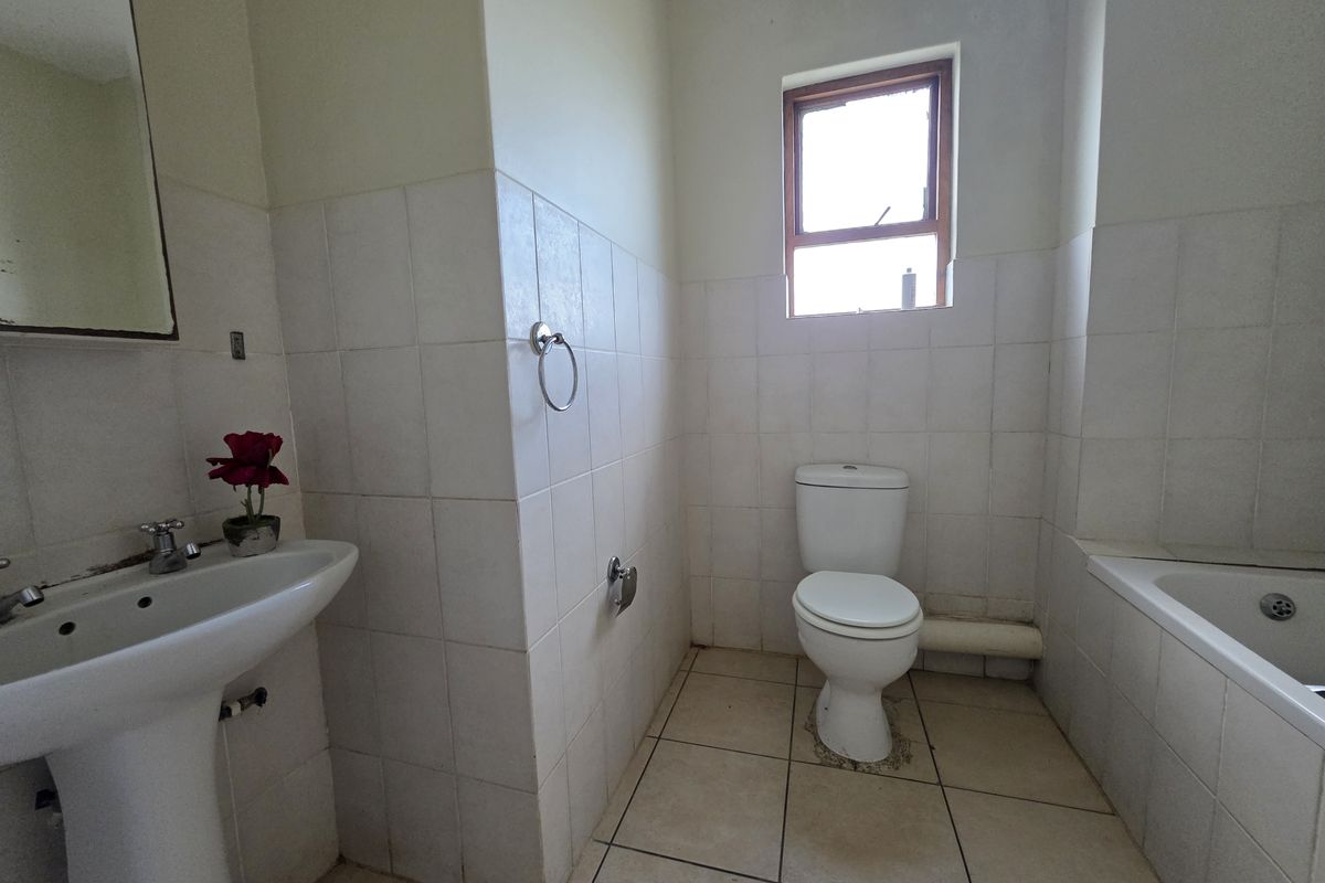 A functional bathroom featuring a pedestal basin, toilet, and bathtub with neutral wall and floor tiling, ready for modernization and cosmetic updates.
