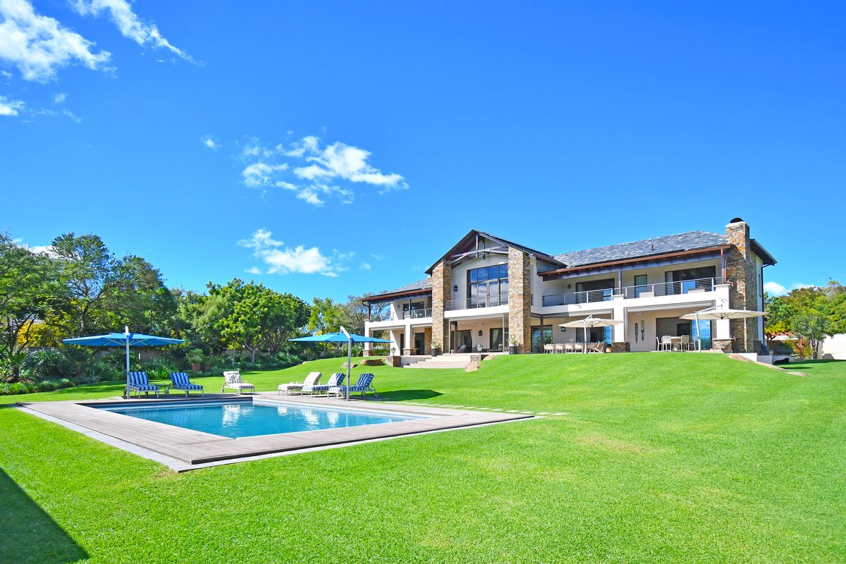 Spacious rear exterior view featuring a large landscaped lawn, a swimming pool with timber decking, and a multi-level residence with stone accents.